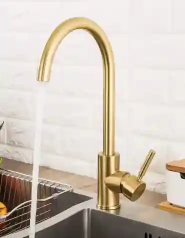 Torneira de cozinha escovado Guimarães com acabamento ouro mate, bica alta arredondada e manípulo lateral cilíndrico, instalada em bancada moderna com fundo branco em azulejo 3D.