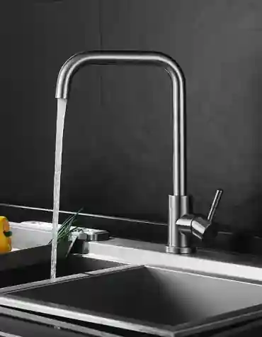 Torneira de cozinha inox escovado Glaciar com bica angular e manípulo lateral, instalada em bancada com lava-loiça inox sob fundo preto texturizado, em ambiente de cozinha moderna.