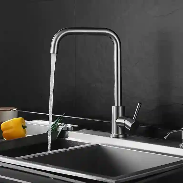 Torneira de cozinha inox escovado Glaciar com bica angular e manípulo lateral, instalada em bancada com lava-loiça inox sob fundo preto texturizado, em ambiente de cozinha moderna.