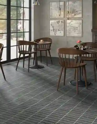 Pavimento cerâmico Kamala 40x60 em tom escuro num café com mesas e cadeiras de madeira